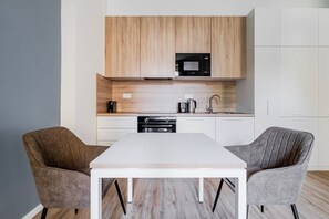 A modern kitchen with wooden cabinets, a microwave, a sink, and two chairs around a white table. - Letná Residence by Blueground (Prague)