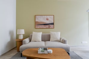 A living room with a sofa, two pillows, a lamp, a coffee table with a book, and a framed picture on the wall. - Nusle Residence by Blueground (Prague)