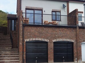 Ein zweistöckiges Gebäude mit Ziegelverkleidung, zwei Garagentoren und einem Balkon mit Sitzgelegenheiten.