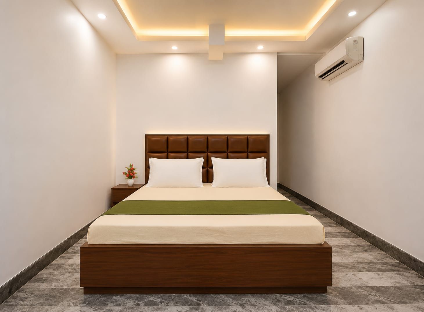 Una habitación de hotel moderna con una cama grande, cabecera de madera, mesita de noche con un florero y un equipo de aire acondicionado en la pared.