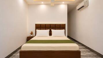 Una habitación de hotel moderna con una cama grande, cabecera de madera, mesita de noche con un florero y un equipo de aire acondicionado en la pared.