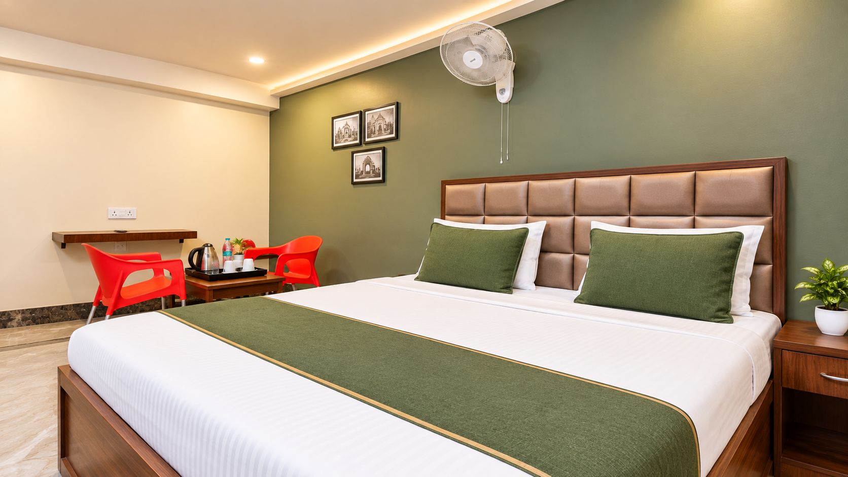 Habitación de hotel con una cama grande, una mesita de noche, un escritorio pequeño y una silla, además de un ventilador de pared.