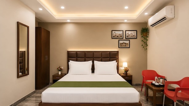Una habitación de hotel con una cama grande, mesitas de noche, un escritorio con sillas y un equipo de aire acondicionado.