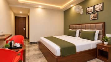 Una habitación de hotel con cama, escritorio, silla, mesita de noche y un ventilador de pared.