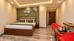 Una habitación de hotel con cama, escritorio, silla, ventilador y una pequeña planta.