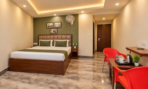 Una habitación de hotel con cama, escritorio, silla, ventilador y una pequeña planta.