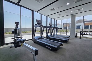 A gym with treadmills and a rowing machine, large windows, and a view of buildings outside. - StayShort - JVC Apartments Sleeps 2 in a Great Location! (JVC)