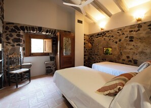 A bedroom with two beds, a wooden chair, a stone wall, and a window.