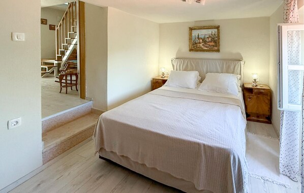 A bedroom with a bed, two bedside tables, a nightstand, a painting on the wall, and a staircase leading to another room. - Gorgeous home in Risika with private swimming pool, can be inside or outside (Risika)