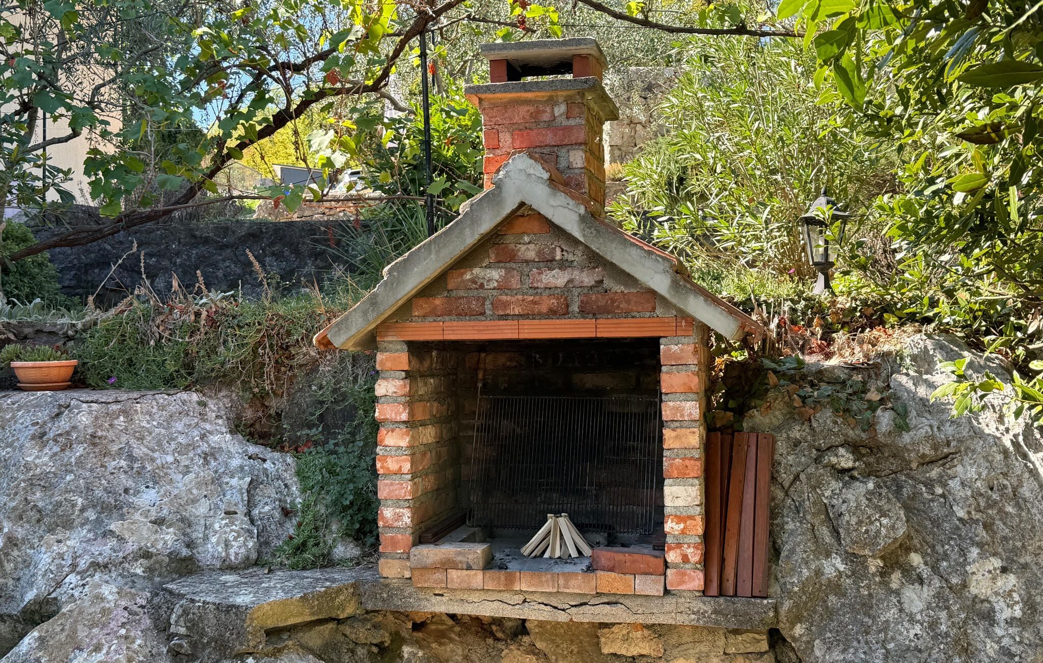 Una pequeña construcción de ladrillo con chimenea, rodeada de follaje y rocas.