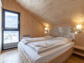 A wooden cabin bedroom with two beds, a large window, and a view of a snowy landscape. - One-bedroom Cabin (Sankt Georgen am Kreischberg)