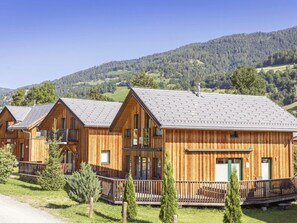 A row of wooden cabins with balconies, set against a backdrop of green hills and a clear sky. - One-bedroom Cabin (Sankt Georgen am Kreischberg)