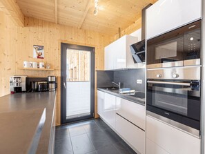 A modern kitchen with stainless steel appliances, wooden walls, and a black tiled floor. - One-bedroom Cabin (Sankt Georgen am Kreischberg)