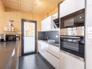 A modern kitchen with stainless steel appliances, wooden walls, and a black tiled floor. - One-bedroom Cabin (Sankt Georgen am Kreischberg)