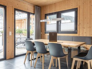 A wooden interior with a table and chairs, large windows, and a view of the outside. - One-bedroom Cabin (Sankt Georgen am Kreischberg)