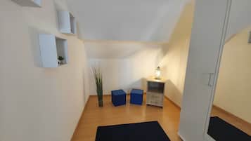Um corredor estreito com piso de madeira, tapete preto, caixa de armazenamento azul, mesa pequena com luminária e guarda-roupa branco.