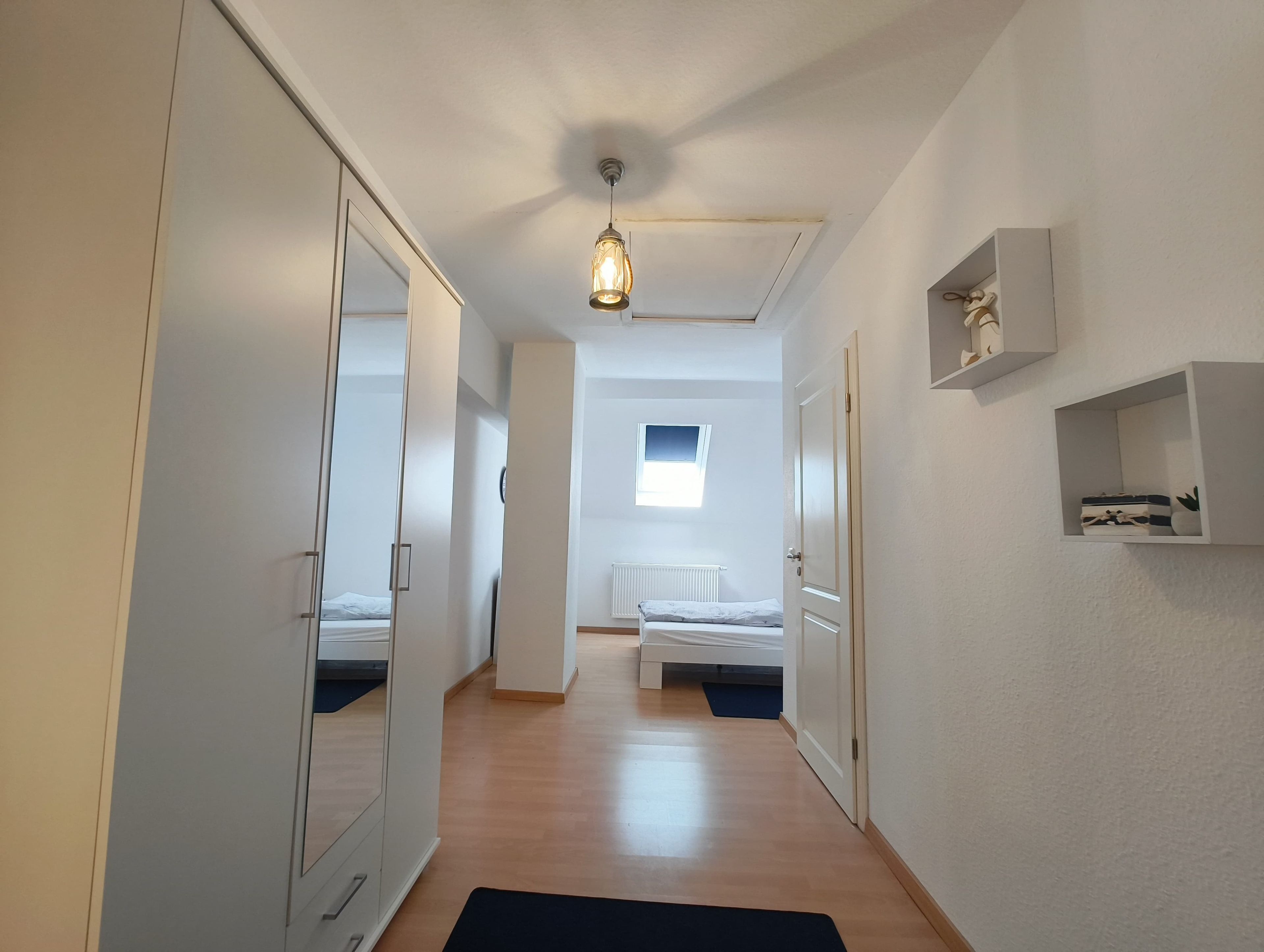 A hallway leading to a bedroom with a bed, a radiator, and a window.