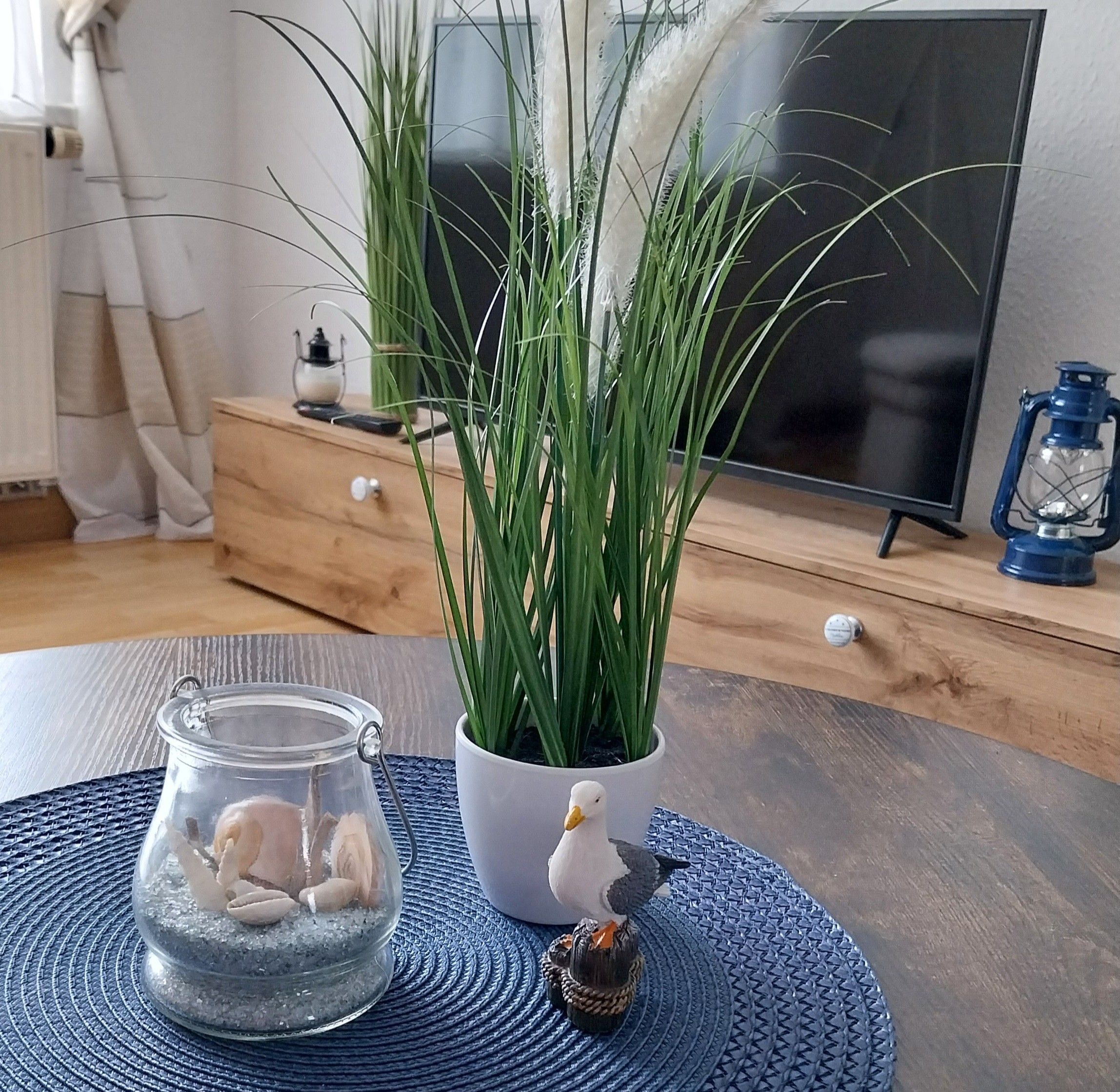 Et værelse med et tv-bord i træ, en potteplante, et glas med sten og en dekorativ fuglefigur.