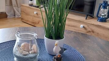 Et værelse med et tv-bord i træ, en potteplante, et glas med sten og en dekorativ fuglefigur.