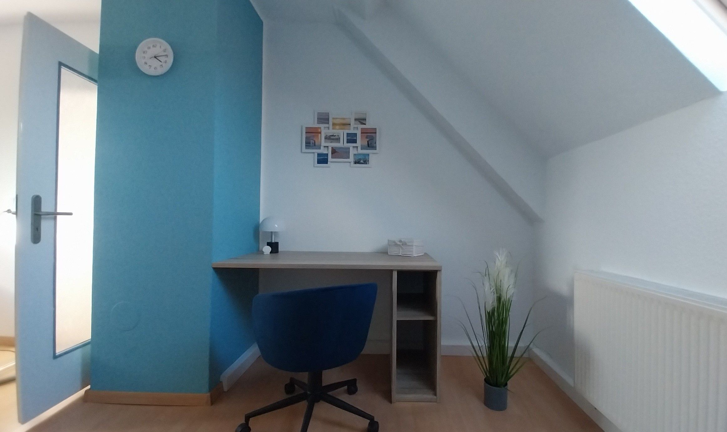 Ein Zimmer mit Schreibtisch, Stuhl und Wanduhr.