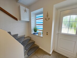 A staircase with a handrail, a window with blinds, a potted plant, and a door with a window.