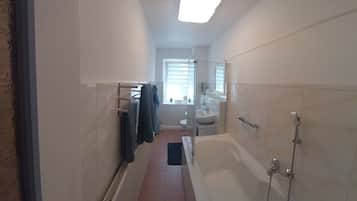 A narrow bathroom with a bathtub, a shower, and a glass-enclosed toilet.