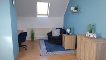 A room with a blue wall, a black leather chair, a wooden cabinet, a small table with a lamp, and a shelf with plants and a sign.