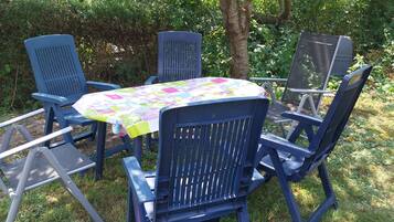 A set of blue chairs and a table with a colorful tablecloth, arranged outdoors with greenery in the background.