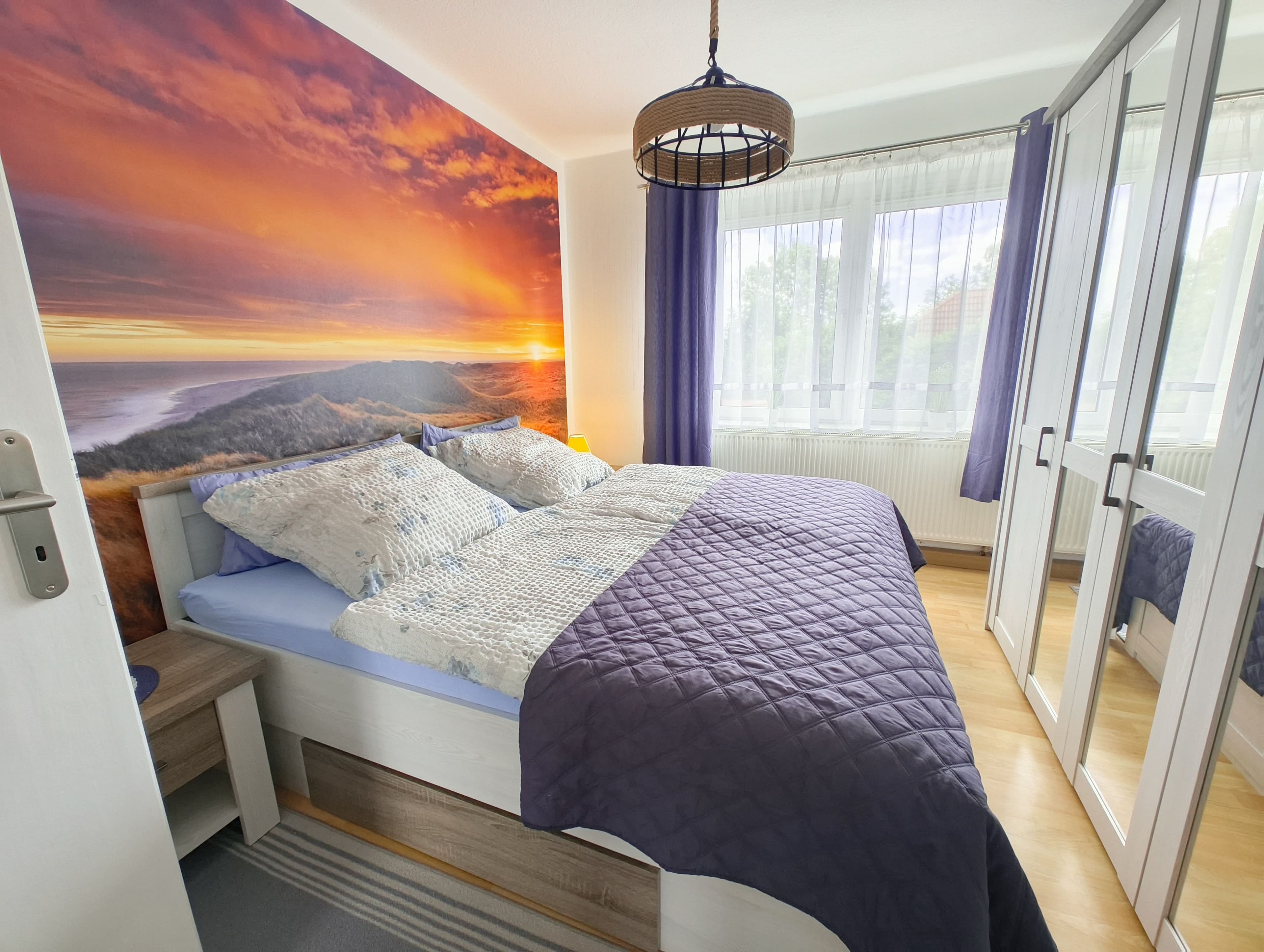 Et soveværelse med en seng, udsigt til solnedgang, en hængende lysarmatur og en skydedør.