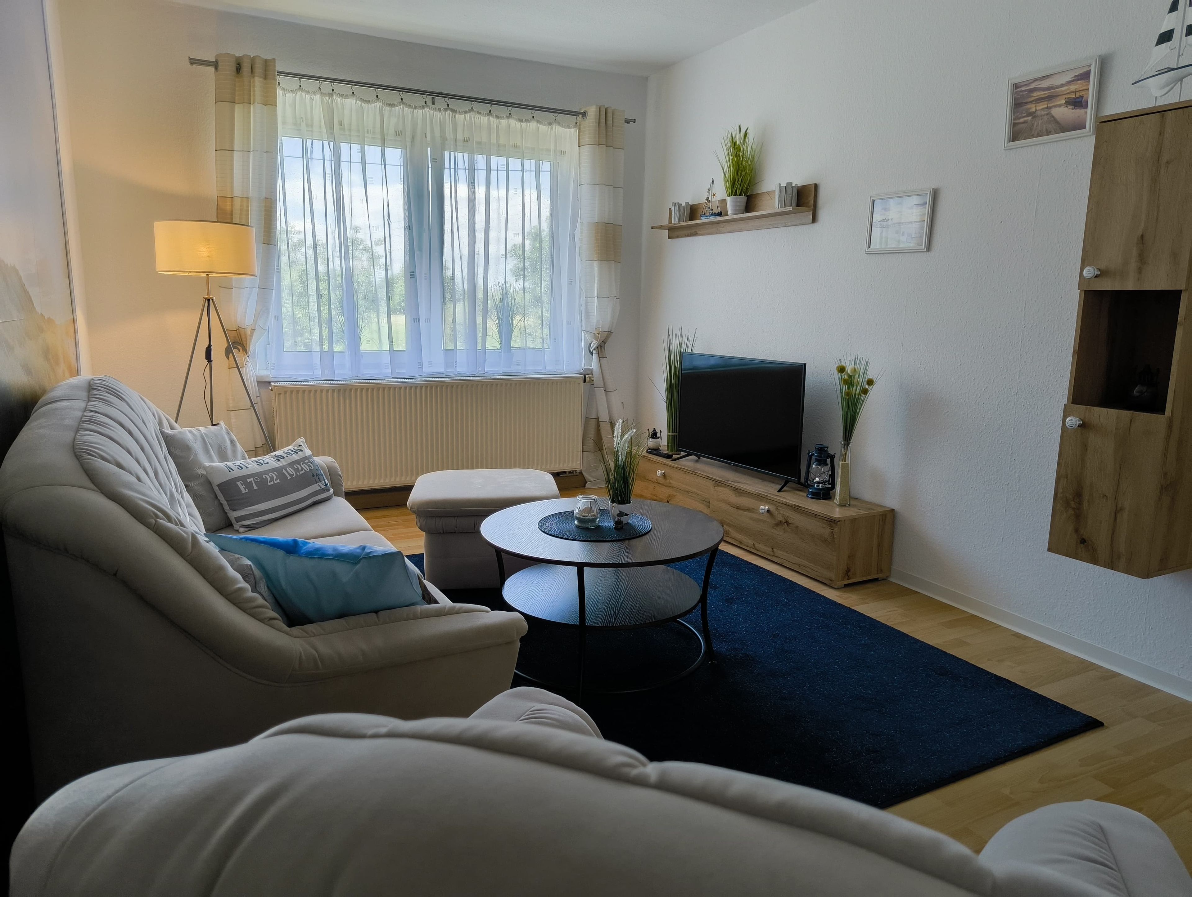 En stue med sofa, sofabord, fjernsyn og et vindue med gardiner.