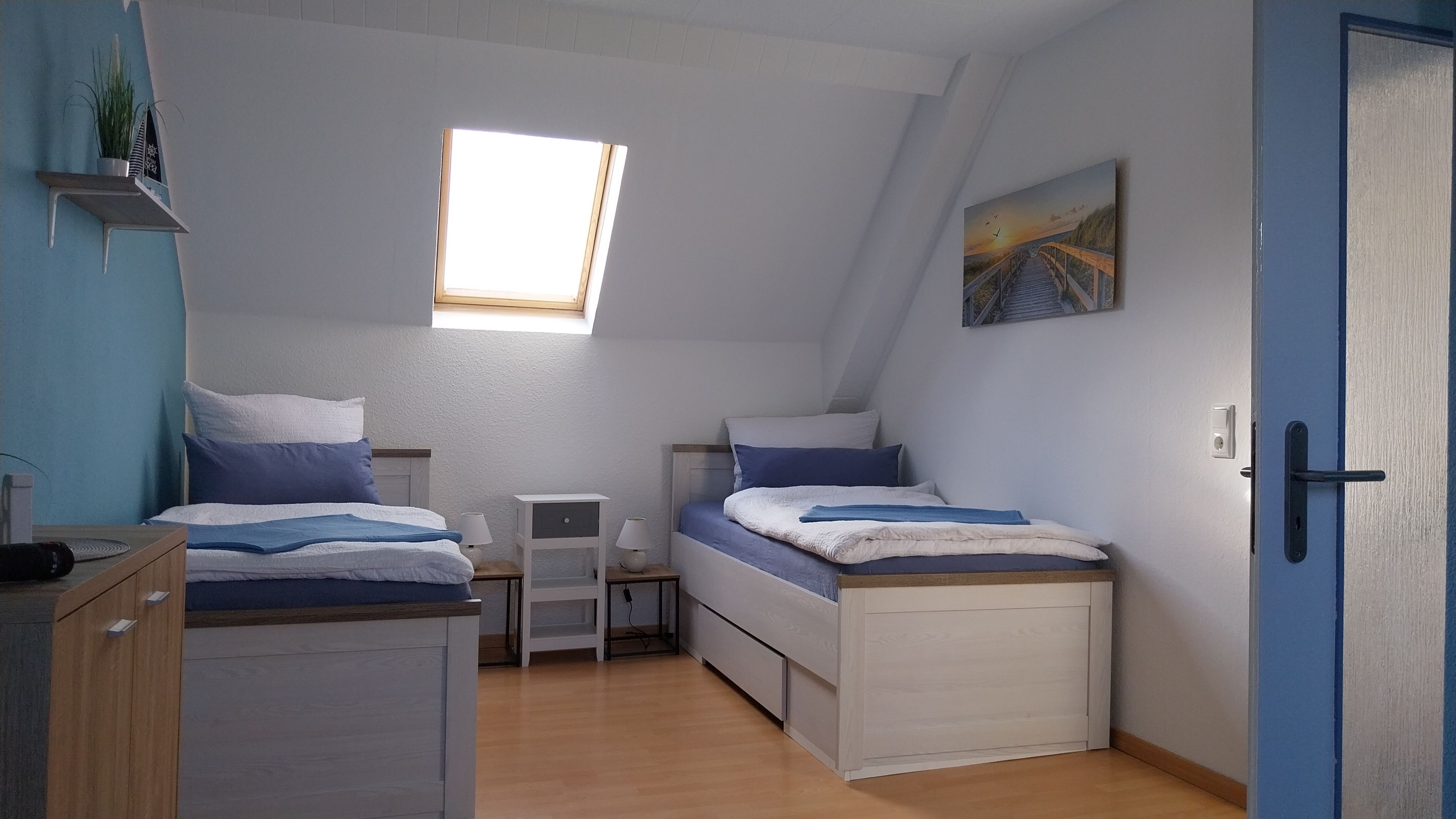 A bedroom with two beds, a window, a nightstand, a lamp, and a door.