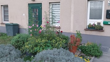 Ein Gebäude mit einer grünen Tür, einem Fenster mit weißem Rahmen und einem kleinen Balkon mit Topfpflanzen.