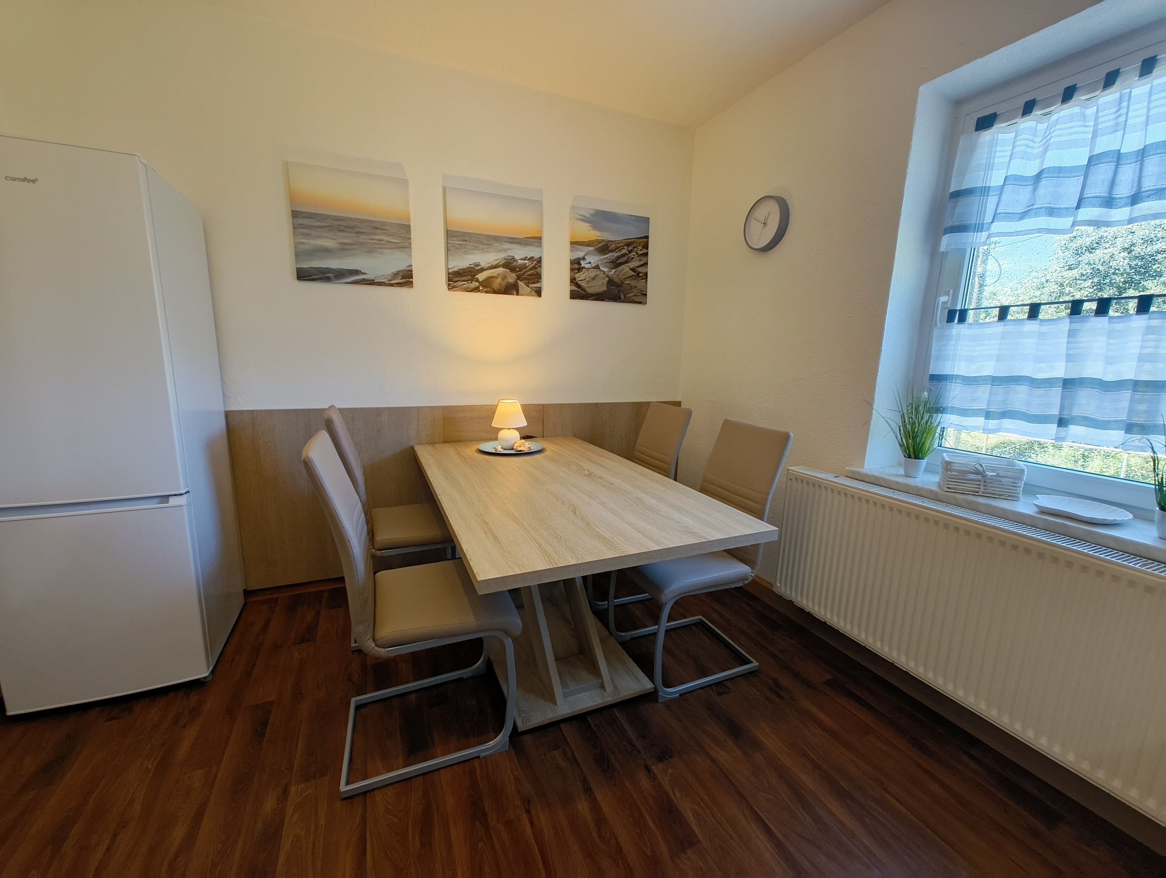 A compact kitchen with a wooden table, chairs, a refrigerator, and a window with a view.
