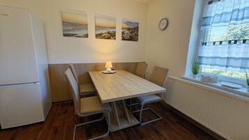 A compact kitchen with a wooden table, chairs, a refrigerator, and a window with a view.