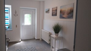 A hallway with a white door, a radiator, a potted plant, and three framed pictures on the wall.