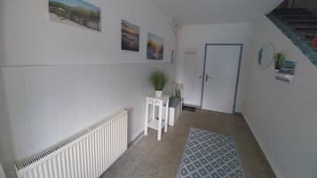 A hallway with a radiator, a door, a small table with a plant, and a patterned rug.