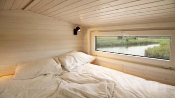 A bedroom with a single bed, a window with a view of a natural landscape, and a wall-mounted light fixture.