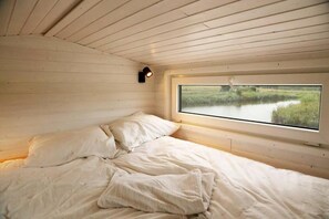 A bedroom with a single bed, a window with a view of a natural landscape, and a wall-mounted light fixture.