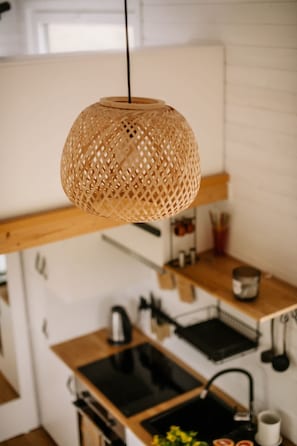 Een keuken met een hangende geweven lamp, houten aanrechtbladen, een zwart fornuis en een witte achterwand.