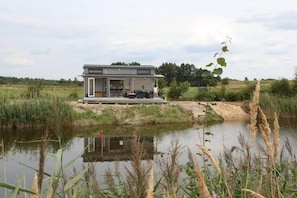 A modern house with a deck overlooking a body of water, surrounded by natural landscape. - Cosy Tiny House by the Water, Close to Nature (Gabrielnia)