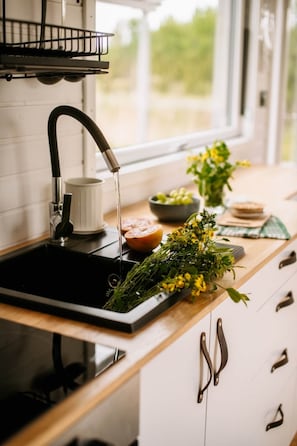 Una cocina con un lavabo negro, una taza blanca, un cuenco de fruta y un ramo de flores amarillas sobre la encimera.