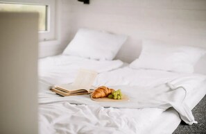 A neatly made bed with a book and a croissant on a wooden tray.