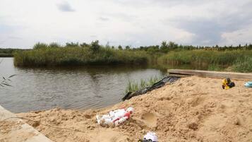 A sandy area with a body of water, some vegetation, and toy vehicles.