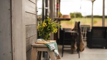 A wooden bench with a potted plant on a wooden stool outside a building.