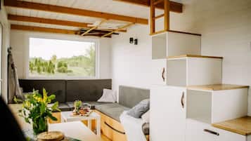 A cozy interior with a sofa, a small table with a vase and a basket, and a window overlooking greenery.