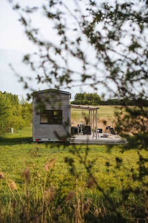 Una cabaña pequeña de un solo piso con un patio, rodeada por un campo de césped y árboles.
