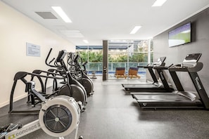 A gym with stationary bikes, treadmills, and a large window offering a view of the outdoors. - Suite 1108 : Spacious CBD 3 Beds +Pool, Gym & Parking (Brisbane City)