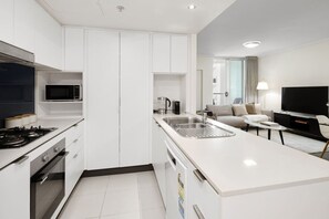 A modern kitchen with a microwave, stove, and sink. There is a dining area with a sofa and a TV. - Suite 1108 : Spacious CBD 3 Beds +Pool, Gym & Parking (Brisbane City)