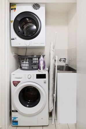 A compact laundry room with a front-loading washer and dryer, a small ironing station, and a sink. - Central Eco-Luxe 2BR, 2BTH • Pool, Gym & Parking (Brisbane City)