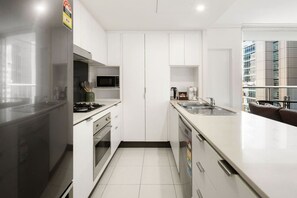 A modern kitchen with white cabinetry, a stainless steel refrigerator, a microwave, and a sink. - Central Eco-Luxe 2BR, 2BTH • Pool, Gym & Parking (Brisbane City)